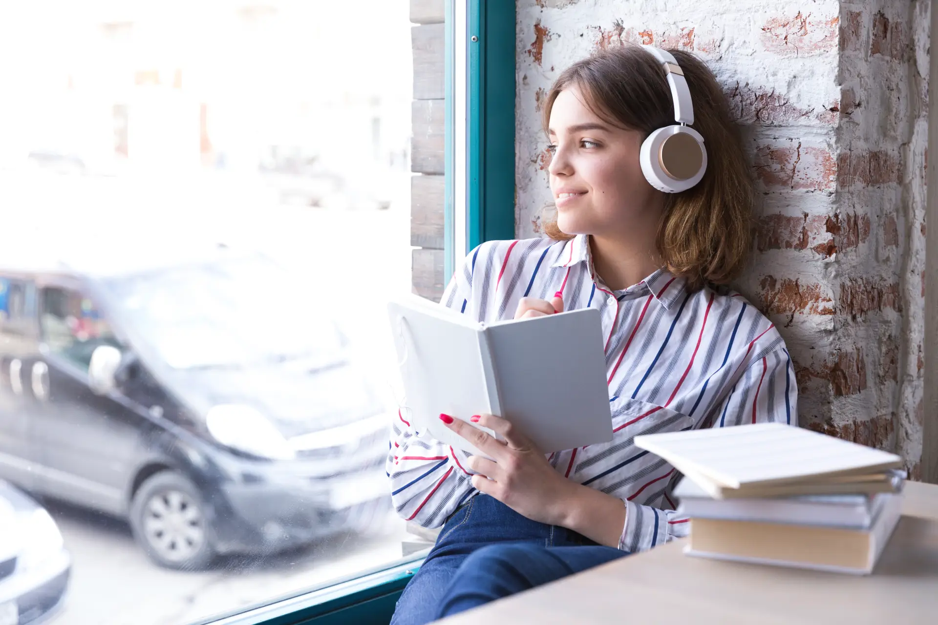 teenager-girl-headphones-sitting-with-open-book-looking-out-window